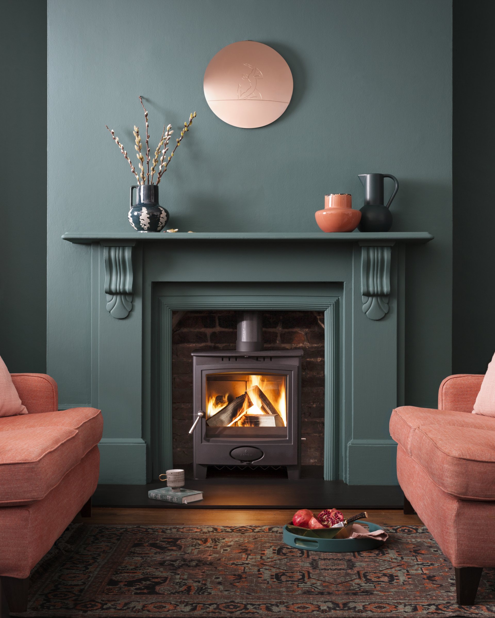Ecoburn Plus 5 Widescreen stove in lit in fireplace in modern room with green walls and peach-coloured sofa and armchair